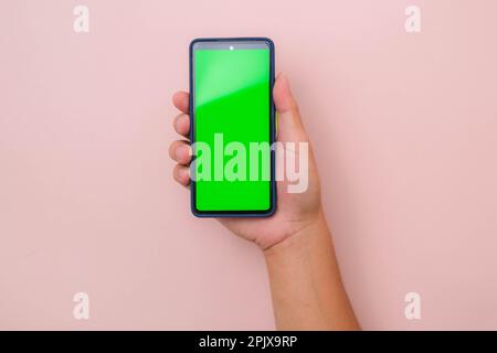 Mobiles Smartphone mit menschlicher Hand und grünem Bildschirm in vertikaler Position isoliert auf pinkfarbenem Hintergrund. Stockfoto