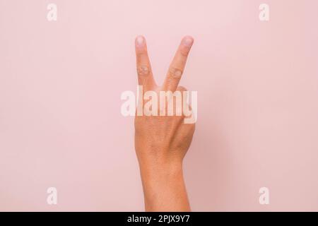 Die Hand zeigt eine Geste mit zwei Fingern (Friedenszeichen) isoliert auf rosa Hintergrund. Stockfoto
