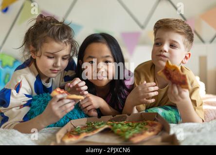 Glückliche Freunde, die auf dem Bett liegen und Pizza essen. Stockfoto