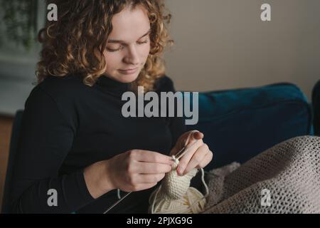 Nahaufnahme-Frau-Porträt-Stricken mit weißem Band und Häkelnadel. Kreative Frauenarme, die ein Handwerk oder Kunstarbeit genießen Stockfoto