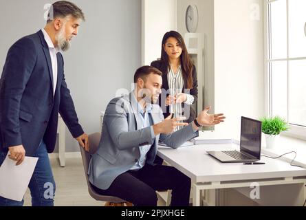 Ein Mann, der mit seinen Kollegen spricht und etwas auf einem Laptop zeigt Stockfoto