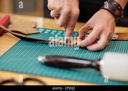 Hände einer Frau, die Löcher in den Ledergürtel macht Stockfoto