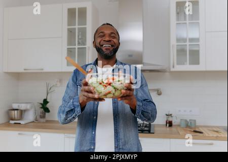 Ein Afroamerikaner hält einen Salat in der Küche. Stockfoto