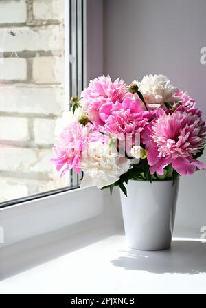 Blick auf einen Strauß rosa Pfingstrosen, der in einer Vase am Fenster steht. Konzepthintergrund, Blumen, Feiertage Stockfoto