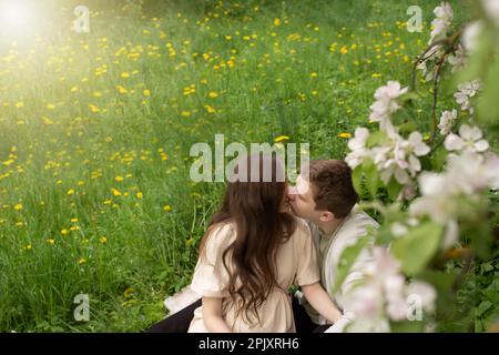 Eine schöne schwangere Frau geht in einem blühenden Garten spazieren. Ehemann, der schwangere Frau umarmt und küsst Stockfoto
