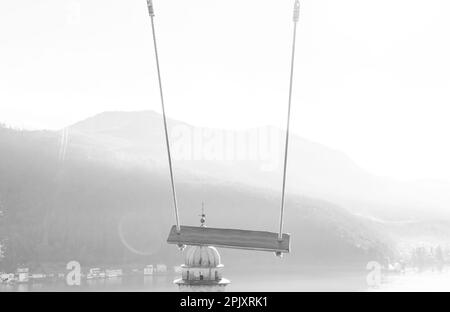 Leere Schaukel mit Bergblick und Sonnenlicht über dem Luganersee in Morcote, Tessin in der Schweiz. Stockfoto