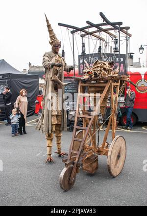 Person auf Stelzen mit einem mobilen Gerät, das einen feuerspeienden Drachen trägt, gesehen auf dem Skipton International Puppet Festival um 2015, Stockfoto