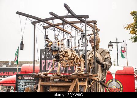 Person auf Stelzen mit einem mobilen Gerät, das einen feuerspeienden Drachen trägt, gesehen auf dem Skipton International Puppet Festival um 2015, Stockfoto