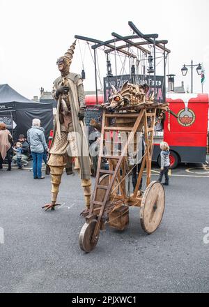 Eine Person auf Stelzen mit einem mobilen Gerät, das einen feuerspeienden Drachen trägt, wie sie etwa 2015 beim Skipton International Puppet Festival zu sehen ist. Stockfoto