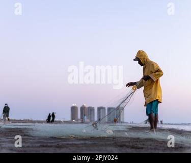 karachi pakistan 2021, ein Fischer in gelber Jacke, der abends Fischernetze für das Angeln mit Meeresblick vorbereitet. Stockfoto