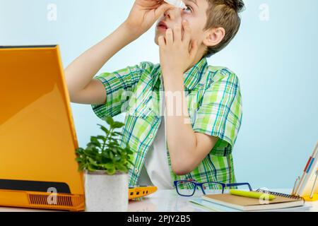 Ein müder Junge fühlt Schmerzen, wenn er seine Augen überanstrengt, weil er am Computer arbeitet. Er tropft gereizte Augen mit Tropfen. Der Begriff der Sehschwäche beim Kind Stockfoto