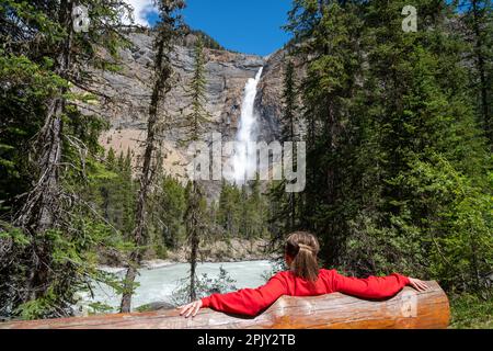 Frau sitzt auf einer Bank und genießt den Blick auf die Takakkaw Falls im Yoho-Nationalpark - British Columbia, Kanada Stockfoto