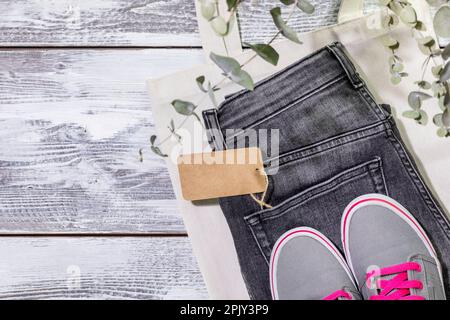 Nachhaltiges Stillleben mit Jeans mit leerem Etikett, Textiltasche und Turnschuhen. Second-Hand-Bekleidungsgeschäft. Kreisförmig, umweltfreundlich, nachhaltig Stockfoto