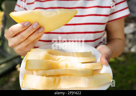 Ein Mädchen in einem gestreiften T-Shirt hält ein Stück gelbe, saftige Melone in den Händen. Sommer, Ruhe, Reisen Stockfoto