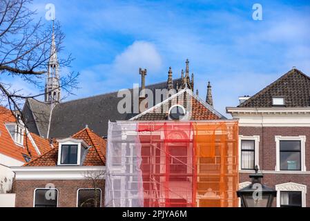Orangefarbenes Gerüst mit Schutznetz gegen historische Gebäude, um zu verhindern, dass Farbe und Baumaterial auf die Straße und Menschen fallen, während Stockfoto