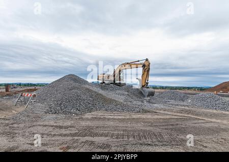 Ein Motorbagger zieht Steine und Kies auf einer aktiven Deponie hoch. Stockfoto