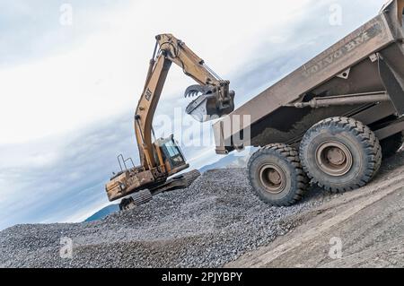 Ein Bagger zieht Steine und Schmutz in der Nähe eines Kipplasters auf einer aktiven Deponie hoch. Stockfoto