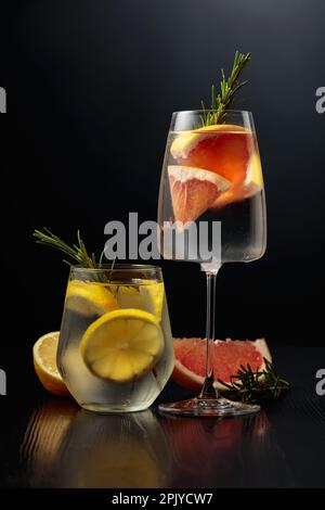Gin Tonic mit Eis, Rosmarin, Zitrone und Grapefruit in Milchgläsern. Gläser mit Cocktails auf einem schwarzen Holztisch. Stockfoto