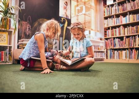 Zwei Grundschulmädchen machen Hausaufgaben in der Schulbibliothek. Schüler lernen aus Büchern. Schüler, die Spaß in der Bibliothek haben. Zurück in die Schule Stockfoto