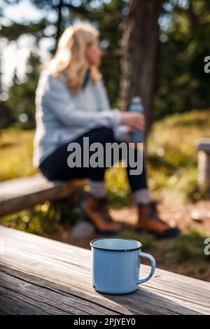 Reisetasse auf Holzbank. Entspannung beim Wandern im Freien. Eine Frau, die im Wald zeltet Stockfoto