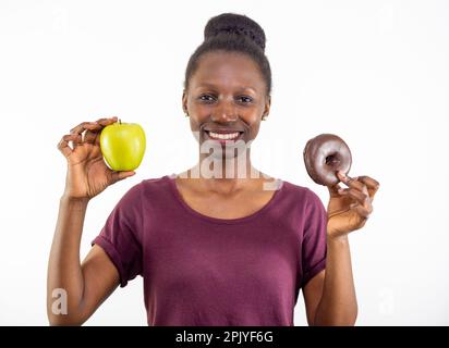 Junge Frau, die sich zwischen gesundem Essen und Junk Food auf weißem Hintergrund entscheidet Stockfoto