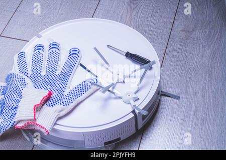 Wartung des Roboter-Staubsaugers. Austausch von Bürsten und Filter. Der Master repariert den Staubsauger. Handschuhe und ein Meisterwerkzeug. Stockfoto