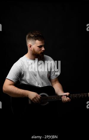 Porträt eines hübschen, bärtigen Mannes mit Brünette, Gitarrist, der eine akustische Gitarre in der Hand hält. Stockfoto