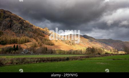 Blick auf die Langdales und das Old Dungeon Ghyll Hotel in Great Langdale mit Harrison Stickle im Sonnenschein und einem Regenbogen weiter oben im vall Stockfoto