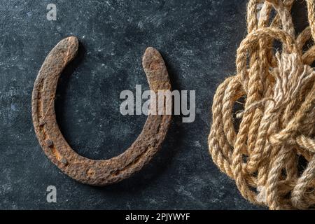 Altes rostiges Hufeisen und Seil auf schwarzem Hintergrund, Nahaufnahme, Draufsicht Stockfoto