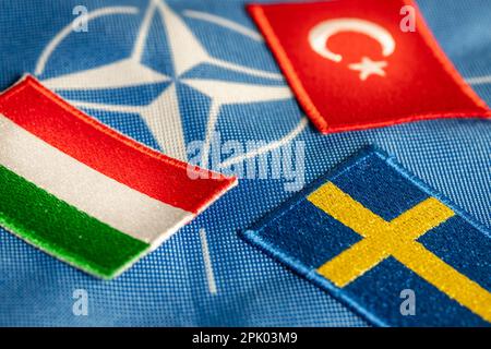 4. April 2023. Türkiye und Ungarn blockieren Schwedens Beitritt zur NATO. Flaggen Schwedens, Ungarns und der Türkei vor dem Hintergrund des Symbos der Verteidigungsallianz Stockfoto