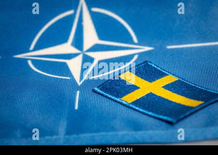 Die Flagge Schwedens vor dem Hintergrund des Symbols der NATO, der Verteidigungsorganisation, dem Konzept der Erweiterung der Grenzen des Bündnisses mit einem Stockfoto