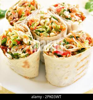 Nahaufnahme von Tortilla Wraps mit Hähnchen und frischem Gemüse auf dem Teller vor hellem Hintergrund. Stockfoto