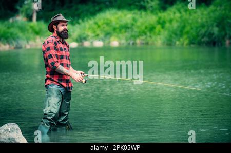 Schöner Mann, entspannt. Sommerwochenenden oder Urlaub. Vereint mit der Natur. Angeln am See. Sommerwochenende. Fliegenfisch-Hobby von Männern in kariertem Hemd Stockfoto