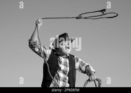 Alter Wilder Westen Cowboy mit Seil. Bärtiger westlicher Mann wirft Lasso mit brauner Jacke und Hut fangen Pferd oder Kuh. Stockfoto