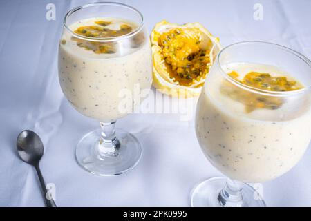 Passionsfrucht-Mousse in einer Glasschüssel, mit Passionsfrucht im Hintergrund, auf weißem Hintergrund. Stockfoto