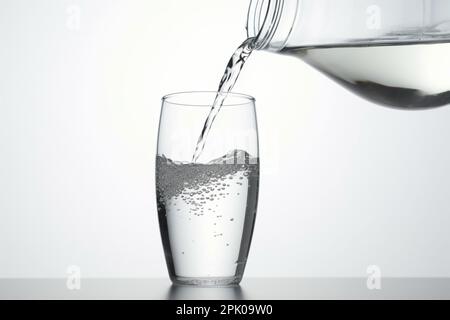 Das Gießen von Wasser aus Flasche in Glas auf weißem Hintergrund Stockfoto