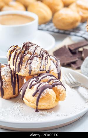 Profiteroles mit Schlagsahne und Schokoladenfüllung, bedeckt mit geschmolzener Schokolade, auf einem Teller, vertikal Stockfoto