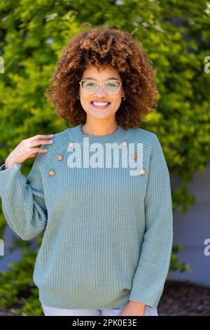 Porträt einer birassischen, schönen jungen Frau mit Afro-Haaren, die lächelt und im Hof steht Stockfoto