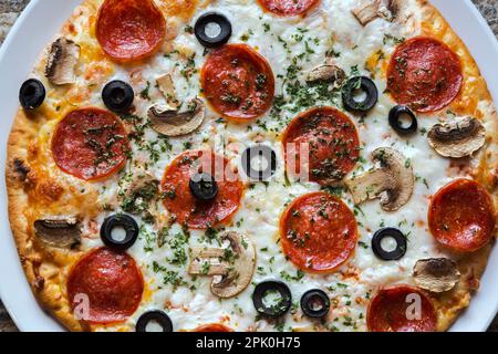 Gebackene Pepperoni- und Käsepizza mit schwarzen Oliven und weißen Pilzen. Stockfoto