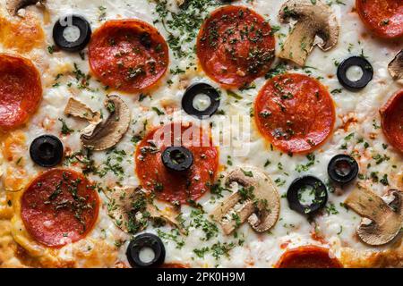 Gebackene Pepperoni- und Käsepizza mit schwarzen Oliven und weißen Pilzen. Stockfoto