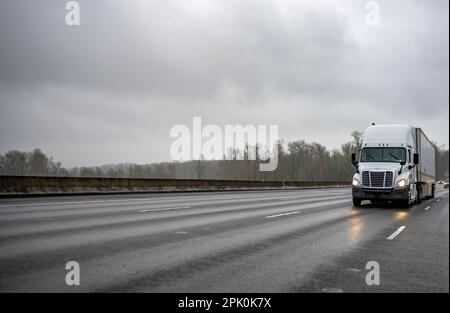 Hohes Fahrerhausprofil weißer langer Transporter großer Sattelschlepper für gewerbliche Fracht im Sattelanhänger für trockene Fracht, der auf nasser Höhe fährt Stockfoto