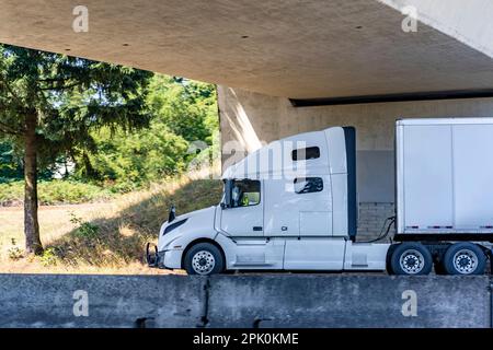 Hohes Fahrerhausprofil weißer langer Transporter großer Sattelschlepper für gewerbliche Fracht im Sattelanhänger für trockene Fracht, der auf dem geteilten Sattelanhänger fährt Stockfoto