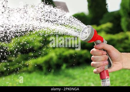 Mann, der Wasser aus dem Schlauch spritzt, im Garten, Nahaufnahme Stockfoto