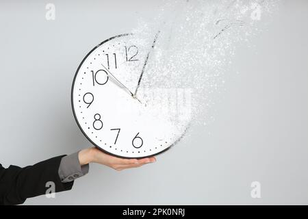 Die Zeit läuft ab. Eine Frau, die vor hellgrauem Hintergrund eine verschwundene Uhr in der Hand hält, Nahaufnahme Stockfoto