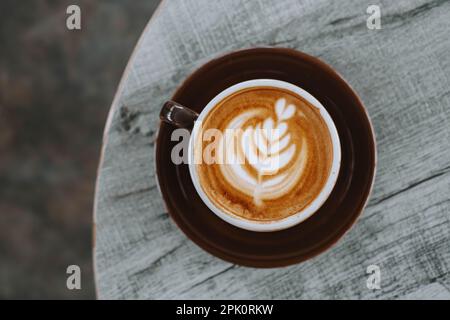 Flach liegend oder mit Blick von oben eine Tasse Kaffee mit wunderschöner Latte Art auf einem Holztisch. Unscharfer Hintergrund. Stockfoto