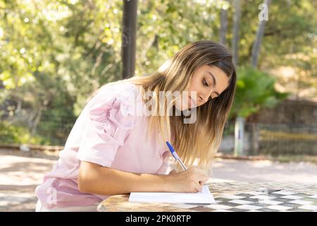 Konzentriertes Teenager-Mädchen, das in ein Buch schreibt. Stockfoto