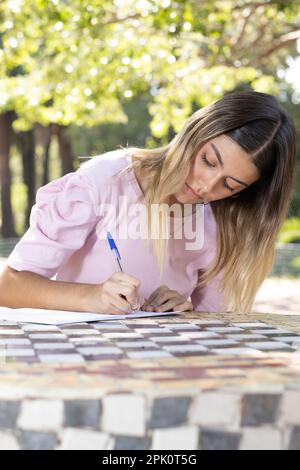 Konzentriertes Teenager-Mädchen, das in ein Buch schreibt. Vertikales Format Stockfoto