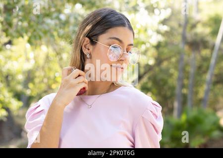 Teenager mit intellektueller Brille und Ohrringen im Ohr, die Parfüm im Park auftragen Stockfoto