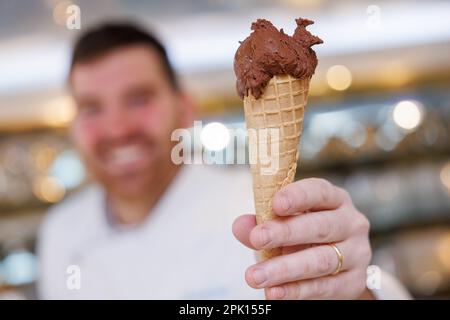 Schwabach, Deutschland. 23. März 2023. Der Eiscreme-Automat Luca de Rocco hält in seinem Eiscafé eine Waffelform mit einer Portion veganem Schokoladeneis. Noch bevor die Eissaison wirklich losgeht, ist eines sicher: Veganes Eis wird weiterhin trendig sein. Aber auf welche neuen Geschmacksrichtungen können sich Eiscreme-Fans dieses Jahr freuen? (Zu dpa: "Fruit Prosecco oder klassische Vanille? The Ice Cream Trends 2023') Kredit: Daniel Karmann/dpa/Alamy Live News Stockfoto