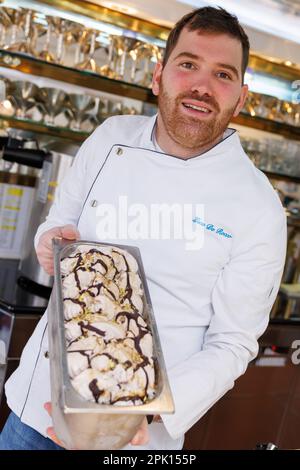 Schwabach, Deutschland. 23. März 2023. Der Eiscreme-Hersteller Luca de Rocco hält in seinem Eiscafé einen Behälter Marzipan-Eis. Noch bevor die Eissaison wirklich losgeht, ist eines sicher: Veganes Eis wird weiterhin trendig sein. Aber auf welche neuen Geschmacksrichtungen können sich Eiscreme-Fans dieses Jahr freuen? (Zu dpa: "Fruit Prosecco oder klassische Vanille? The Ice Cream Trends 2023') Kredit: Daniel Karmann/dpa/Alamy Live News Stockfoto